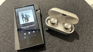 Technics EAH-AZ100 无线耳塞，在灰色表面的音乐播放器旁边